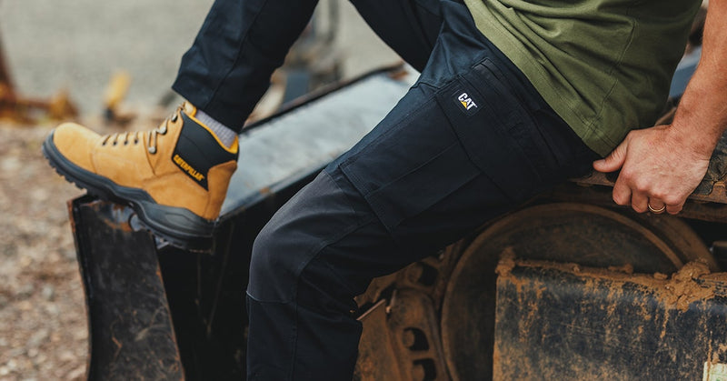 Close-up image of a man sat on plant machinery, wearing a pair of black Caterpillar Dynamic Trousers